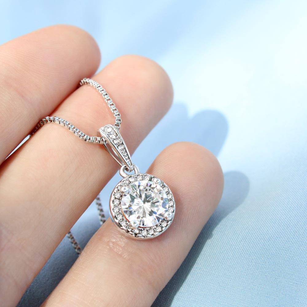 Silver-tone round halo cubic zirconia pendant on a thin link chain, held in hand