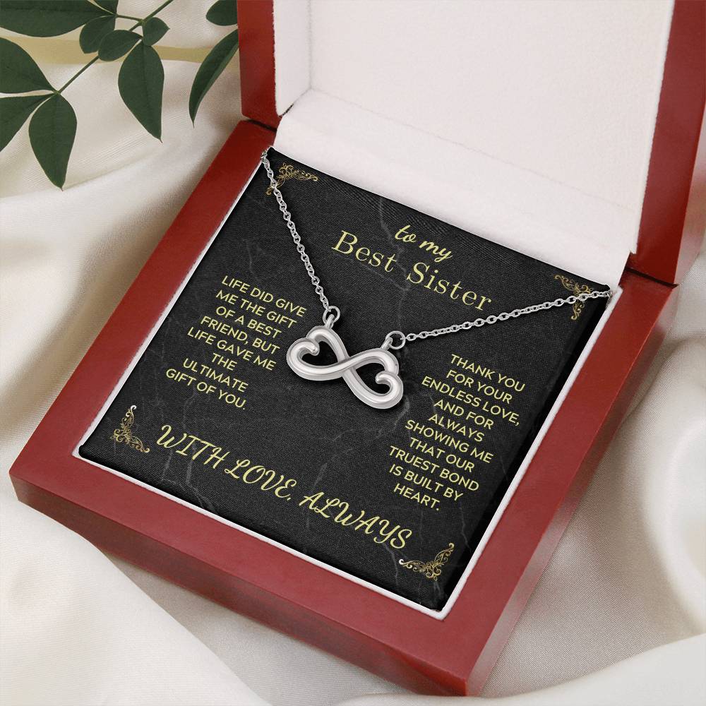 Infinity heart pendant necklace on a black “Best Sister” card inside an open box