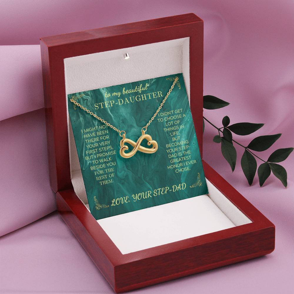 Gold heart infinity necklace resting on green message card in a wooden gift box