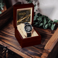 Open wood watch box holding black leather open-work wristwatch and DAD message card