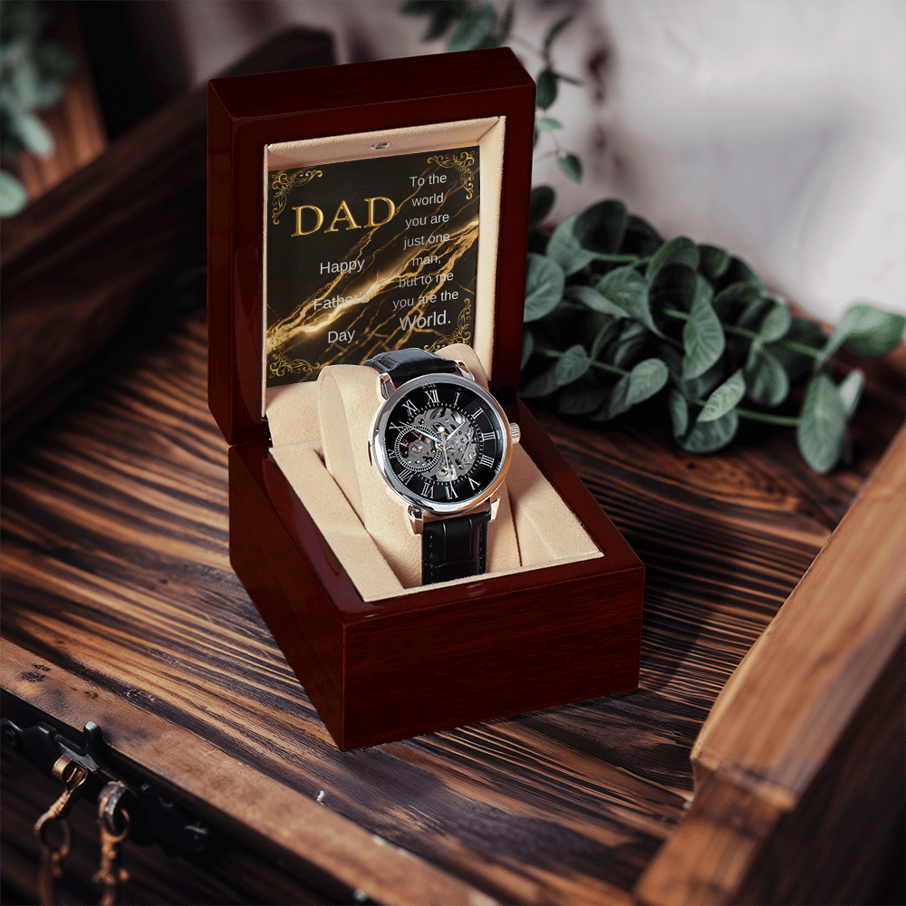 Open wood watch box holding black leather open-work wristwatch and DAD message card
