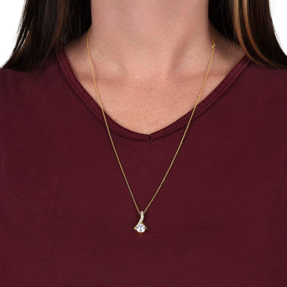 Gold-tone necklace with teardrop crystal pendant, worn on a burgundy top