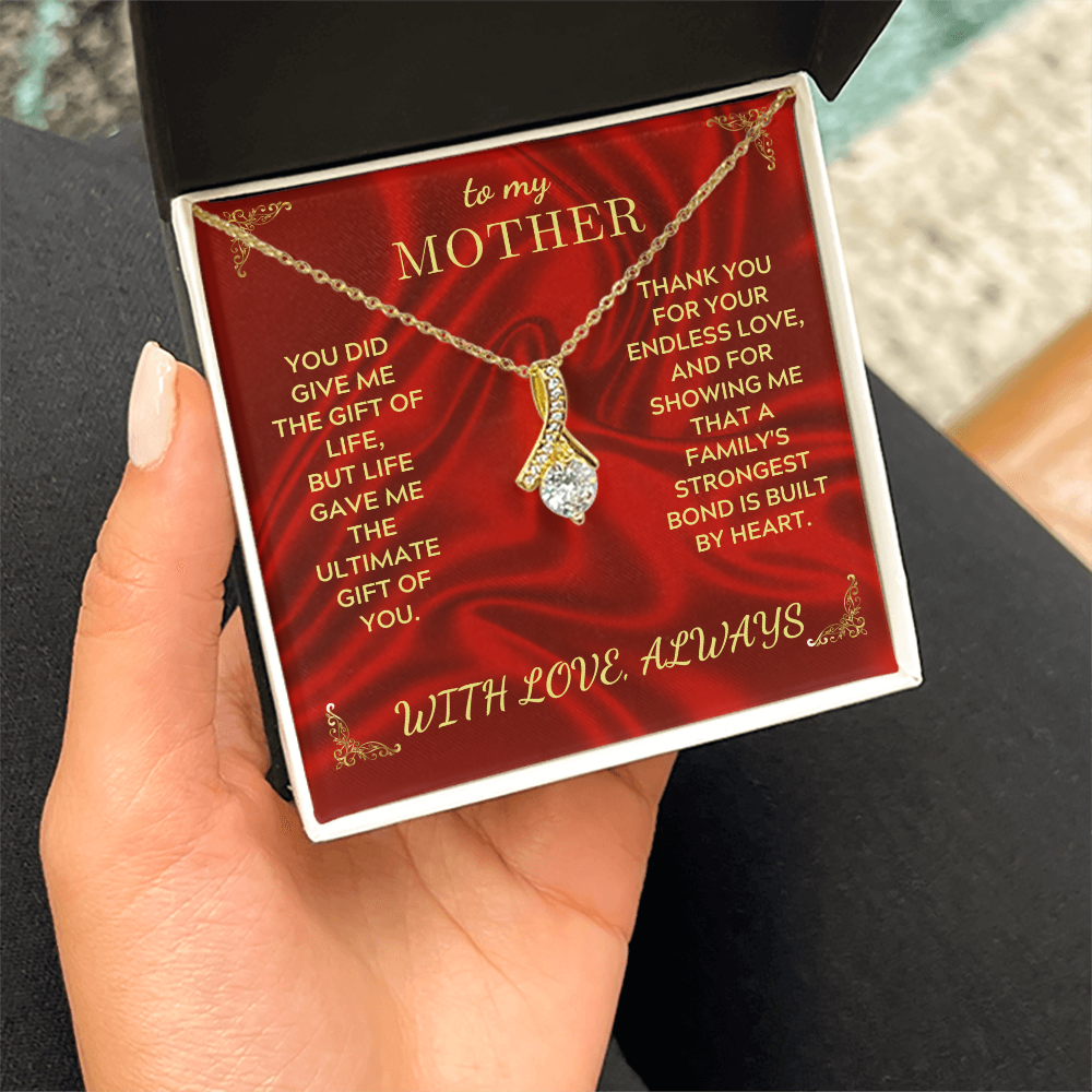 Gold necklace on hand with teardrop heart pendant above open red gift box