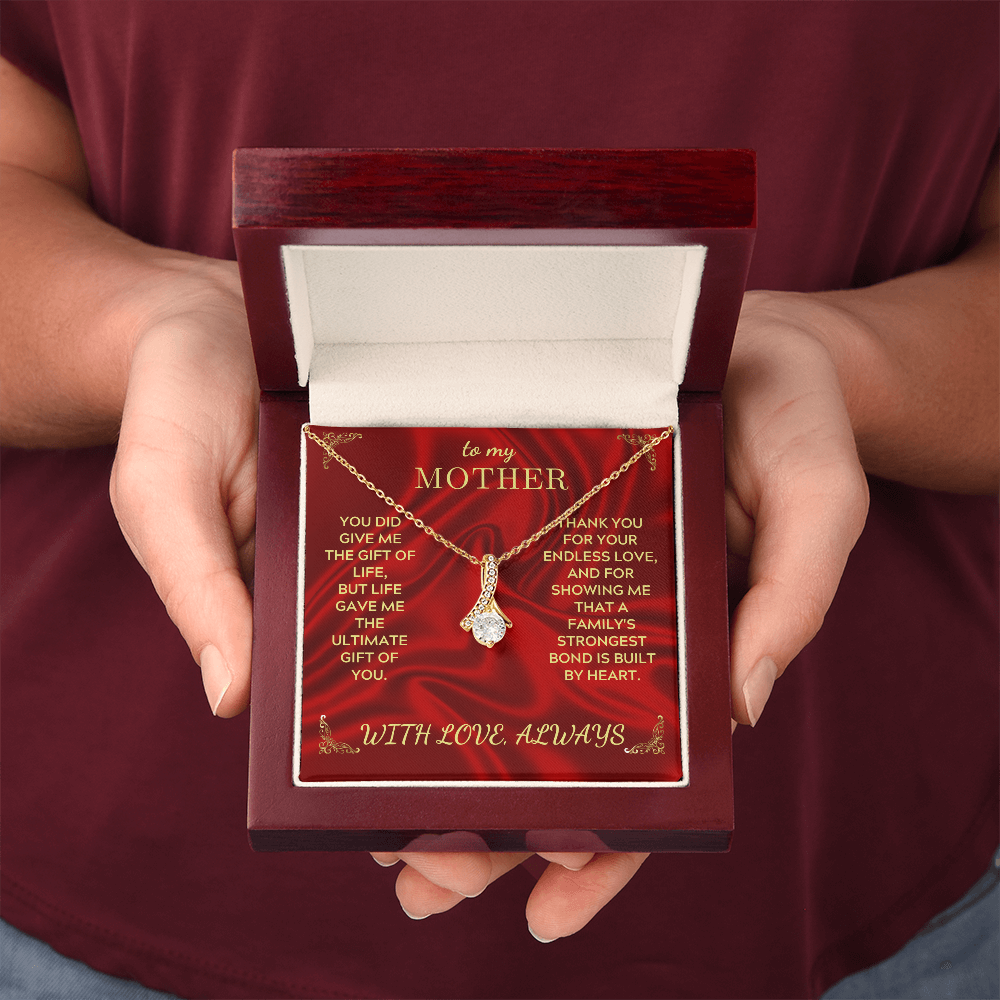 Hands holding open necklace gift box with red 'To my Mother' card and gold-tone pendant