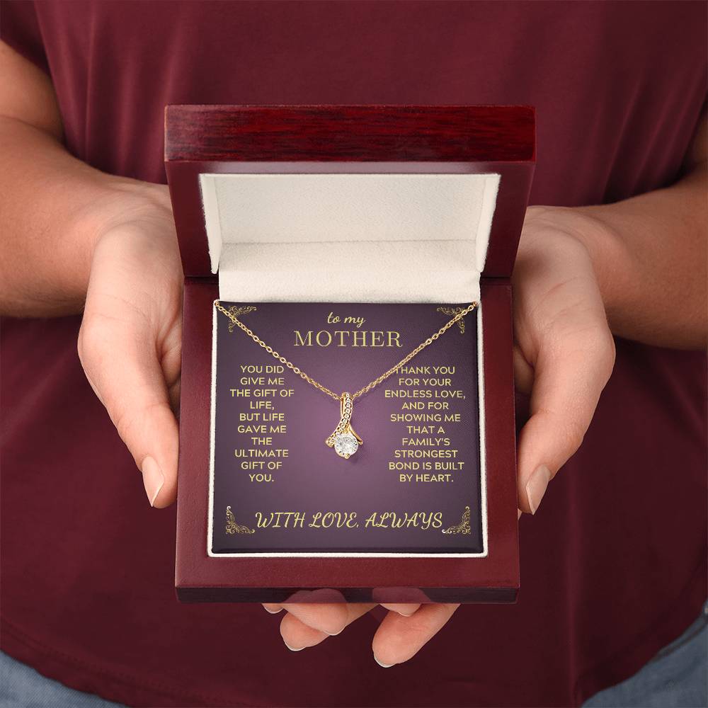 Closed gift box held up by hands, gold-tone necklace with teardrop crystal pendant on purple insert