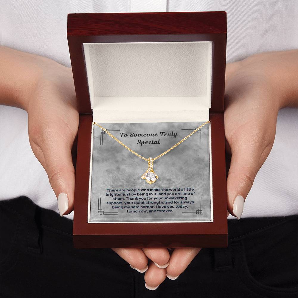 Gold-tone necklace with teardrop pendant held above maroon gift box