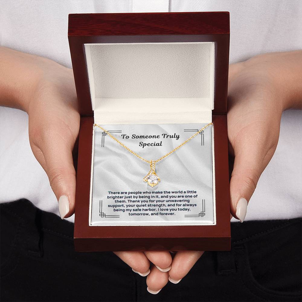 Gold tone pendant necklace displayed in burgundy gift box held in hands