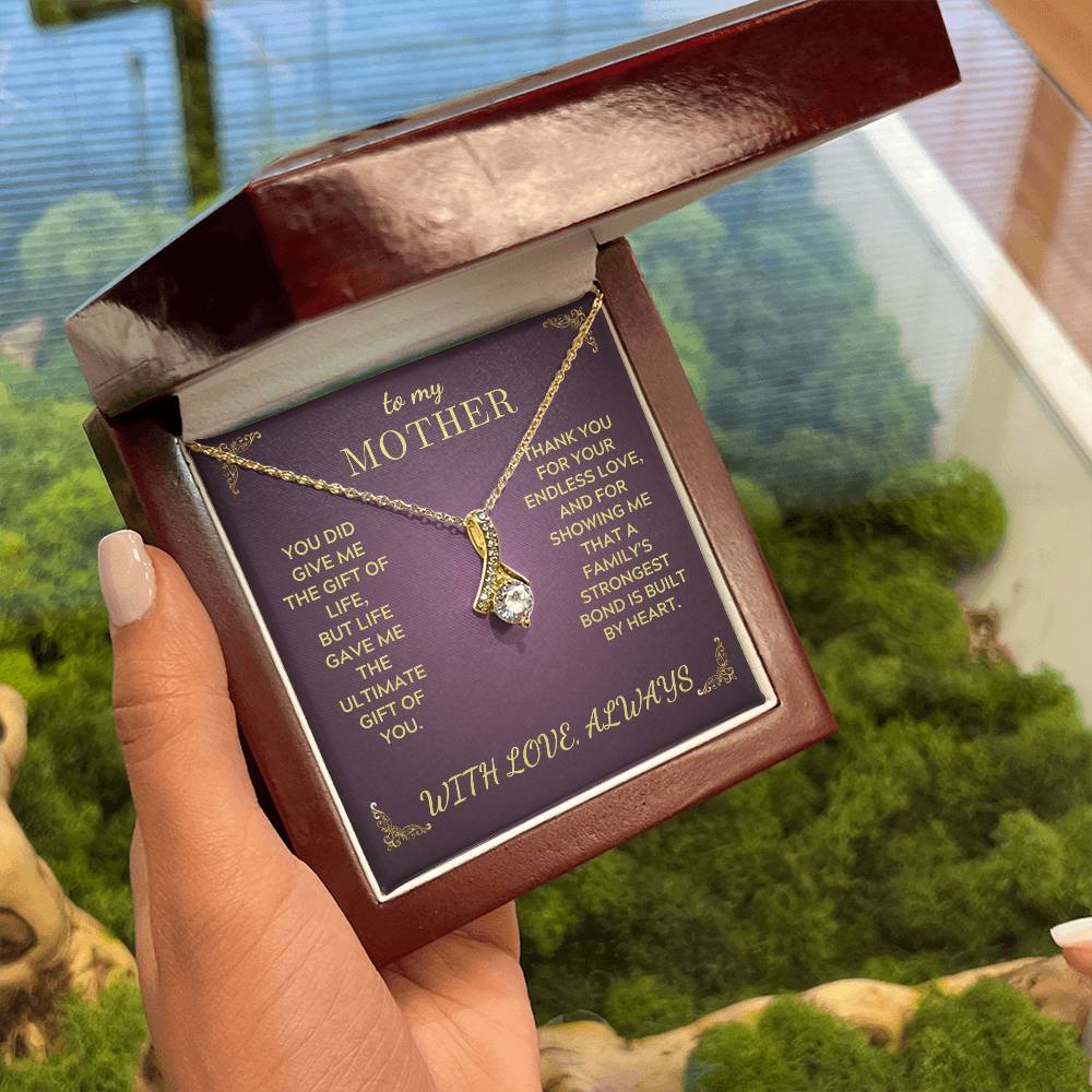 Gold-tone necklace shown in open gift box with teardrop crystal pendant on purple insert