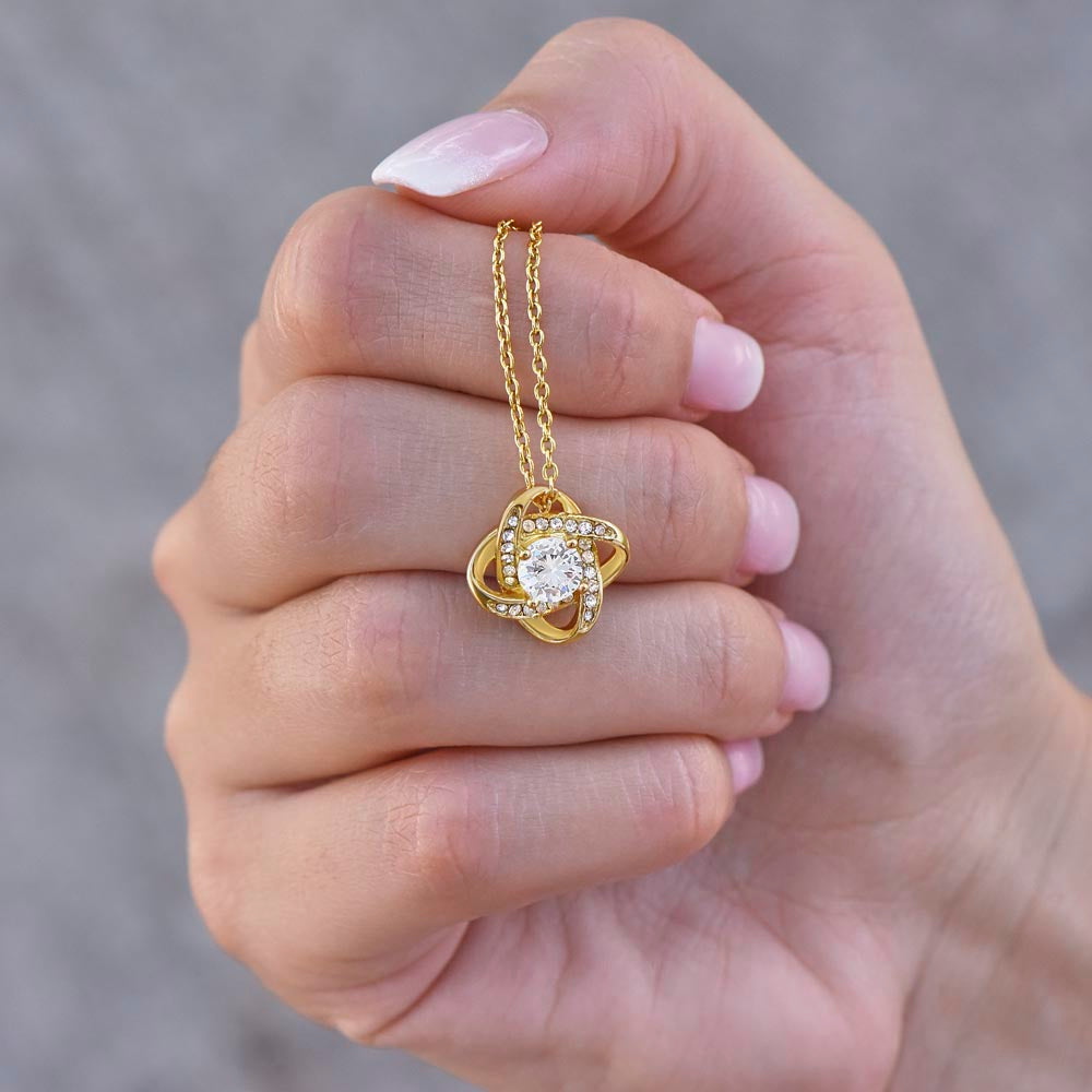 Gold heart-shaped love knot pendant necklace with rhinestone details held in hand