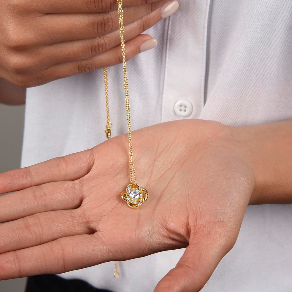 Love knot necklace pendant on gold-tone chain held over open palm