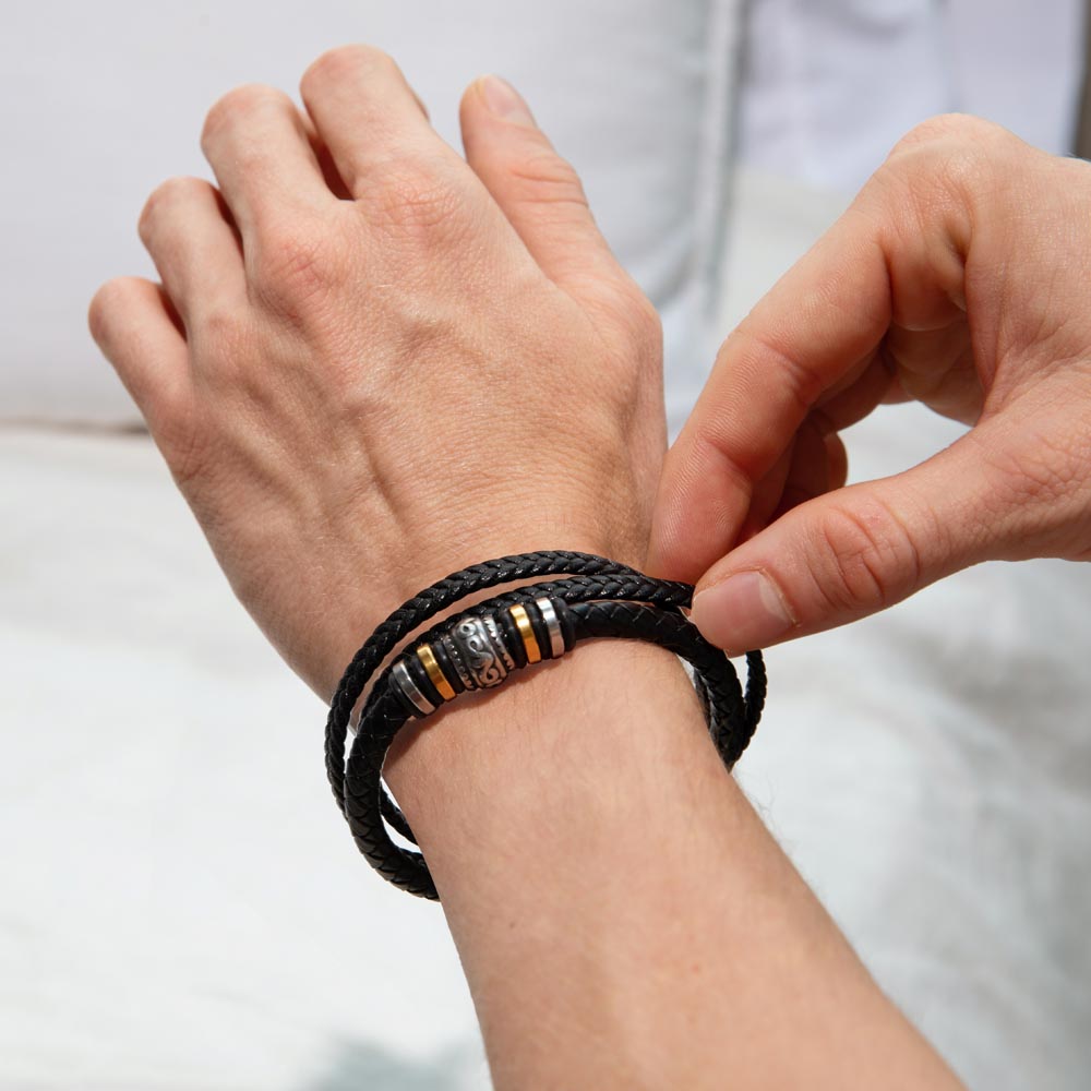 Man’s hand wearing a black braided bracelet with gold and silver bead accents