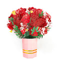 Red paper flower bouquet with green leaves and yellow accents in pink striped vase