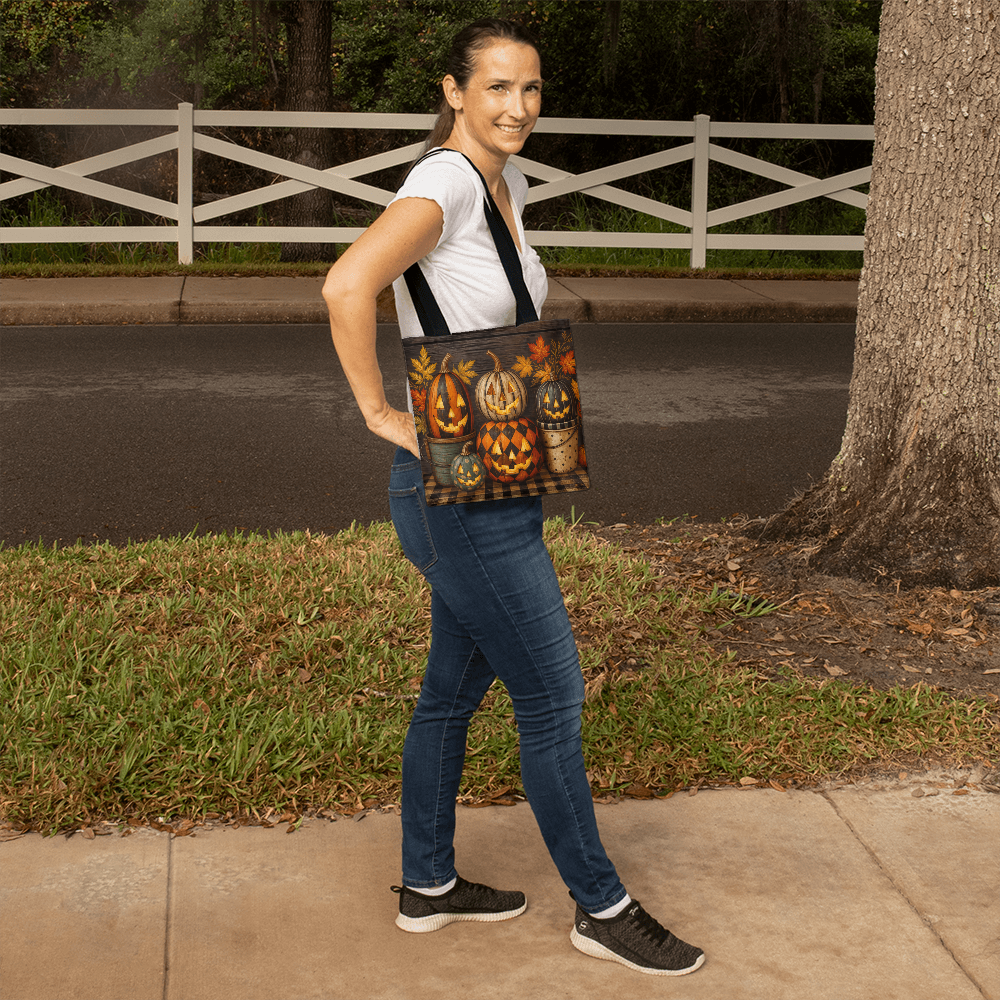 Black-handled dark canvas tote bag with pumpkin jack-o’-lantern print, carried by model