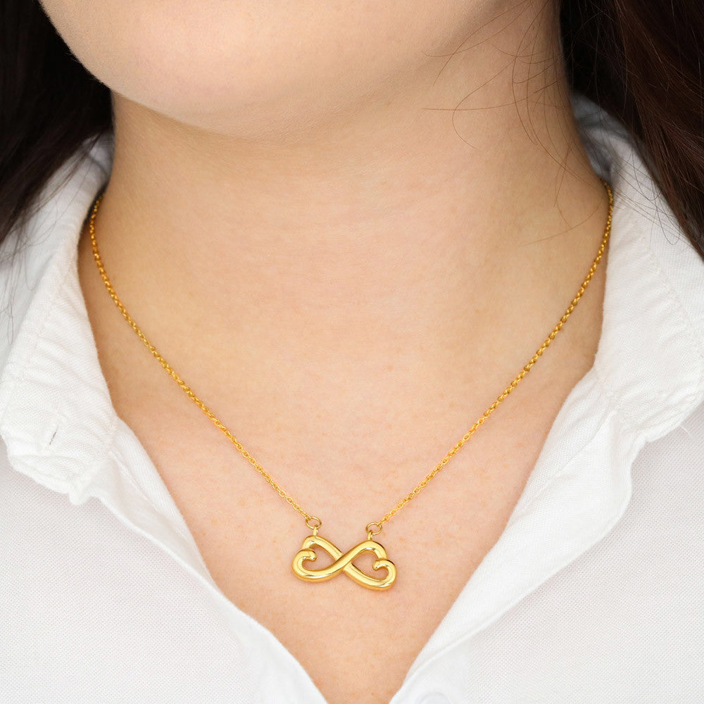 Gold heart infinity pendant necklace on a white blouse neckline.