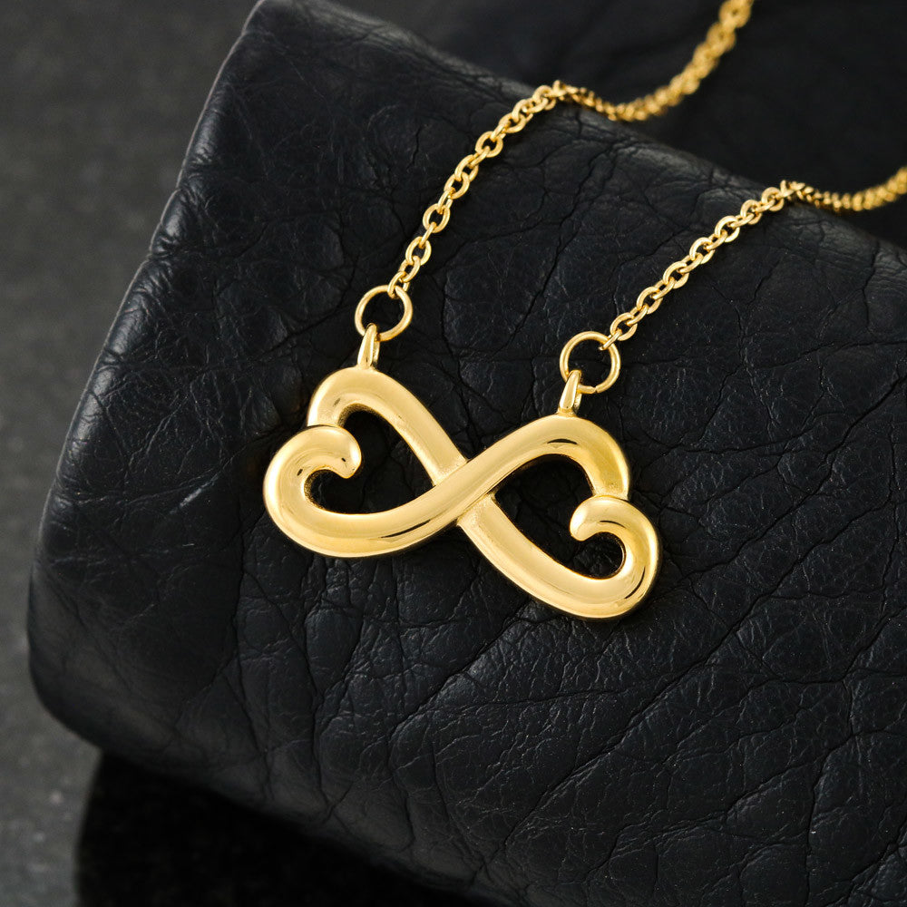 Gold infinity heart pendant necklace with link chain, close-up on dark textured surface