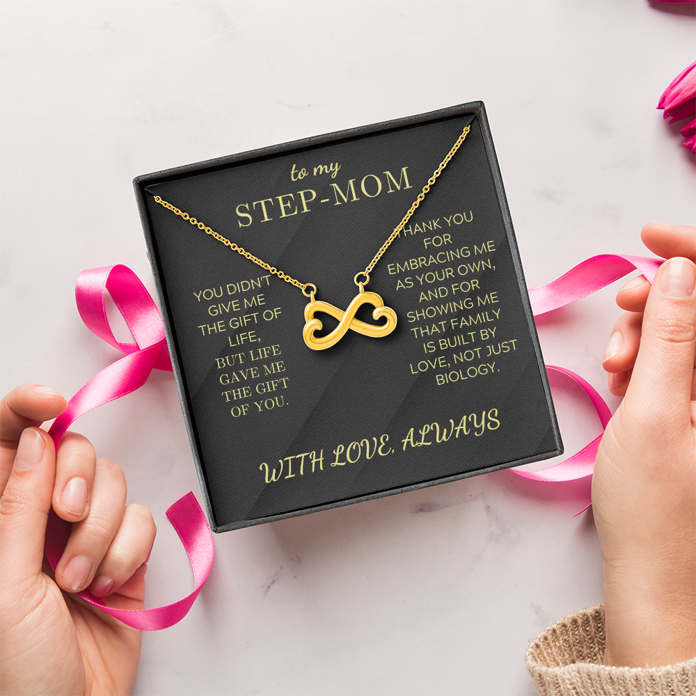 Gold infinity heart pendant necklace in a black gift box with pink ribbon and hands