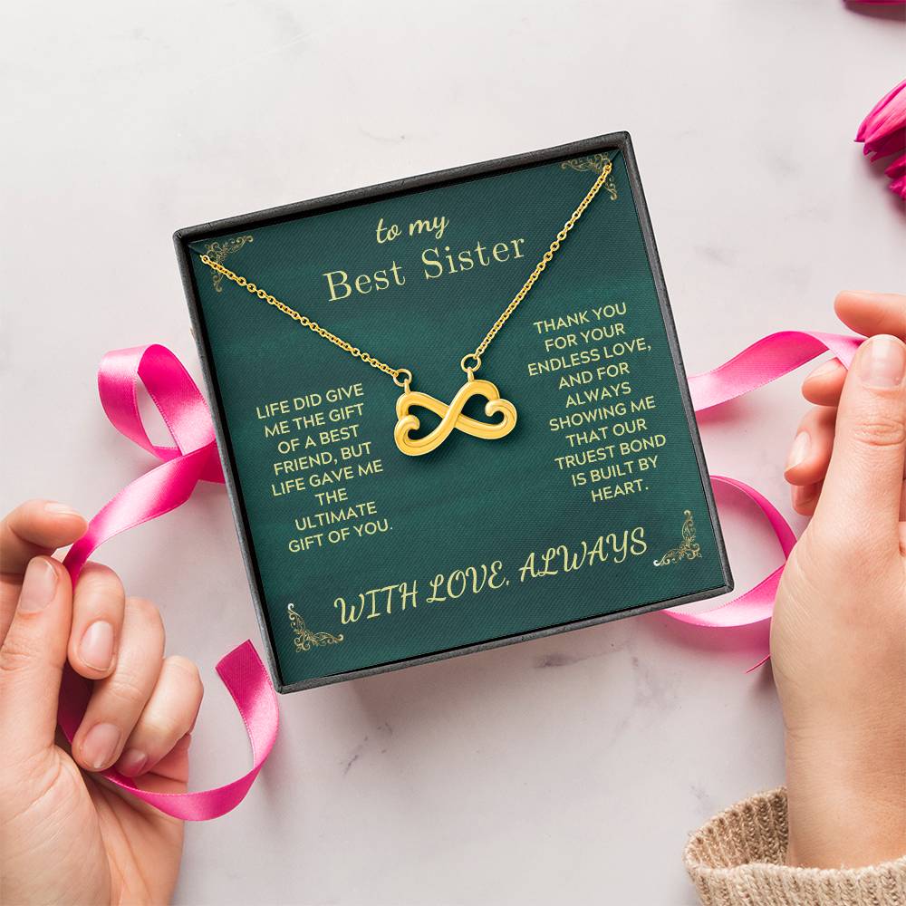 Green gift box with gold heart infinity pendant necklace tied with pink ribbon.