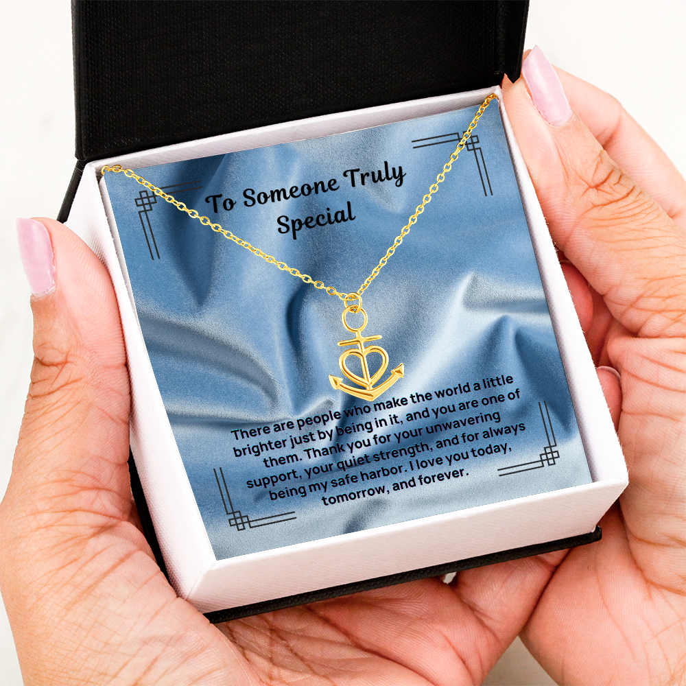 Gold anchor and heart pendant necklace on a chain in a gift box, held in hands.