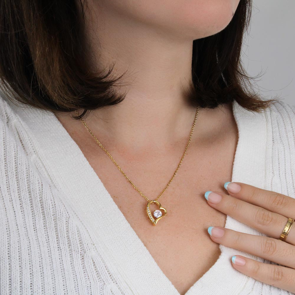 Gold tone heart pendant necklace with round zirconia charm worn on neckline