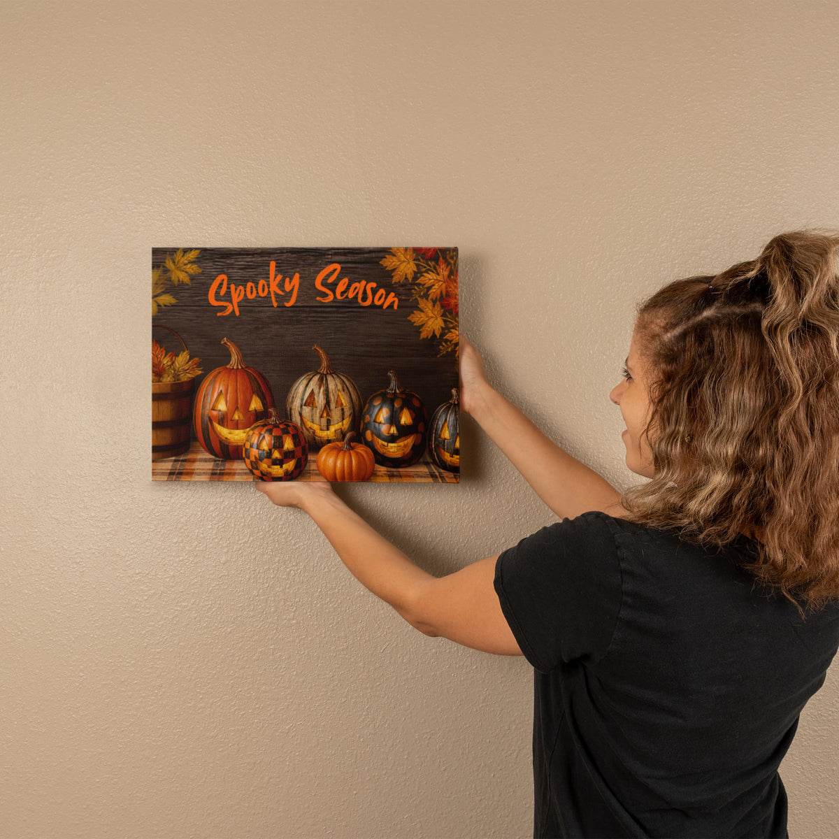 Woman holding Halloween pumpkin canvas print with orange “Spooky Season” lettering